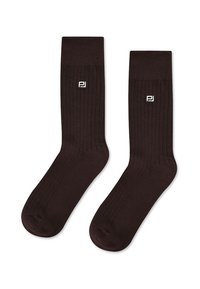 Brązowe rajstopy prążkowane o miękkiej fakturze i podwiniętym końcu, z małym białym logo z boku. Odpowiednie zarówno na co dzień, jak i na bardziej formalne okazje.