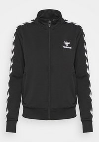 Black zip-up jacket with high collar, featuring white chevron stripes on sleeves and a small Hummel logo on the upper left side.