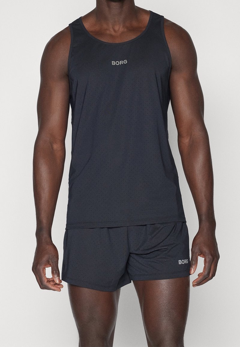 Homme portant un haut de sport noir sans manches et un short assorti avec des logos "BORG" sur la poitrine et le short, sur fond uni.