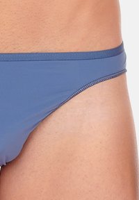 Blaue Schwimmslips mit glatter Textur, schmalem Bund und dezenten Nähten. Sie verfügen über einen klassischen Schnitt, der sich zum Schwimmen eignet.