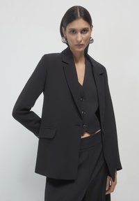 Blazer nero su misura con colletto elegante, chiusura a singolo bottone e tasche frontali. Presenta una texture liscia e una vestibilità strutturata.