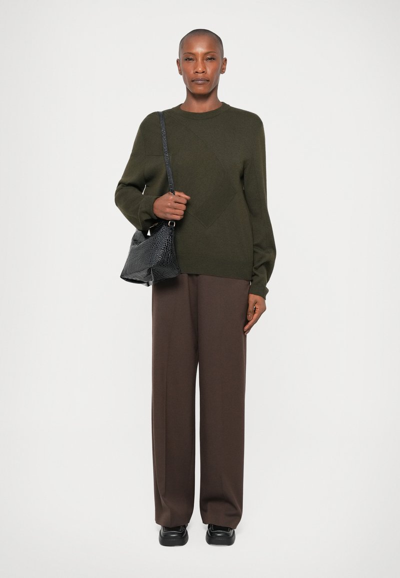 Pull en maille vert olive avec un motif diagonal texturé, associé à un pantalon large marron et un sac à main en simili-cuir crocodile noir.