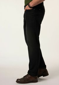 Vaqueros de mezclilla negra con corte recto, que cuentan con bolsillos frontales y una sutil textura desgastada. Combinados con zapatos marrones de cordones.