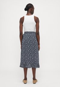 Jupe midi florale avec ourlet à volants, base bleu foncé, motif floral blanc. Associée à un débardeur blanc et des chaussures à enfiler beiges.