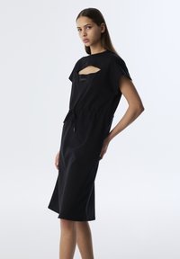 Schwarzes Kleid mit kurzen Ärmeln, das an der Brust über einen Ausschnitt verfügt und einen verstellbaren Taillenbund hat. Glatte Textur, knielanges Design.