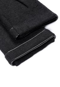Gants en laine noir avec bords surpiqués et finitions en cuir, pliés sur un fond blanc, montrant une texture et un savoir-faire détaillés.