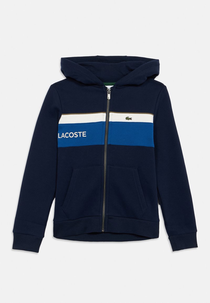 Hanorac cu fermoar de culoare albastru marin, cu dungi orizontale albe și albastre, buzunare frontale, glugă și logo Lacoste cu text pe piept.