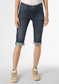 Dunkelblaue Denim-Shorts mit taillierter Passform, umgeschlagenen Säumen und frontalen Taschen, kombiniert mit beigen Sneakers vor einem neutralen Hintergrund.