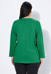 Zielony T-shirt z długim rękawem wykonany z miękkiej bawełny. Posiada okrągły dekolt i luźny krój, z prostymi rękawami i dołem sięgającym poniżej talii.