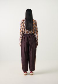 Mönstrad skjorta i orange, svart och vitt; lösa mörka byxor; träplattforms skor med röda accenter; långt rak hår.