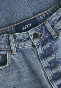 Traperice s plavim i svijetlim pranjem, s kontrastnim tamnim pranjem na prednjem dijelu džepa i JJXX oznakom.