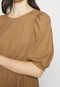 Vestido marrón texturizado con mangas abullonadas cortas y un cuello redondo, que presenta una cintura fruncida y una tela suave con estampado.