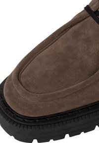 Scarpa in suede marrone con punta arrotondata, dettagli cuciti e suola in gomma nera robusta con modelli di battistrada testurizzati.