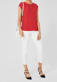 Rød kortærmet bluse med udskæringsdetalje, parret med hvide cropped jeans og sorte stiletter, kompletteret med en lille hvid håndtaske.