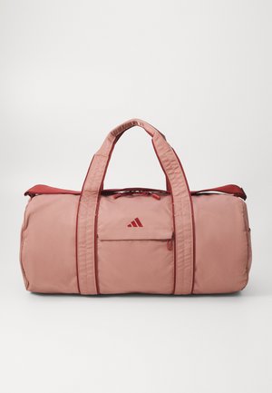 Bolsa de deporte rosa con acentos rojos, que presenta asas resistentes, un bolsillo frontal y un cierre con cremallera. Fabricada en un tejido duradero y suave.