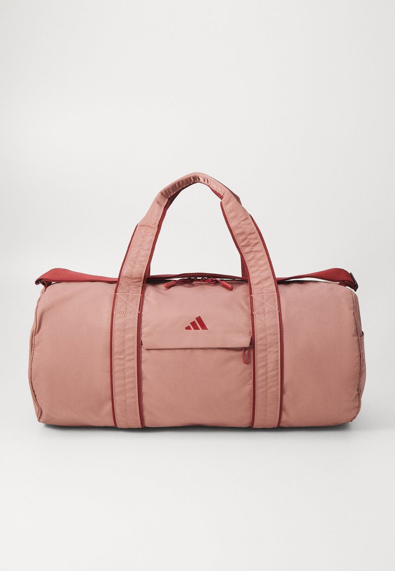 Sac de sport rose avec des accents rouges, doté de poignées robustes, d'une poche avant et d'une fermeture éclair. Fabriqué à partir d'un tissu durable et lisse.