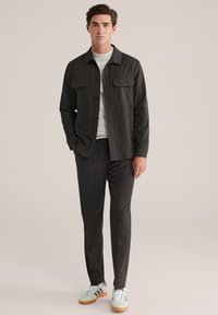 Sötétszürke gombos dzseki, két mellzsebbel, sötétszürke, testre szabott nadrággal és világoszöld sportcipővel, fehér részletekkel párosítva.