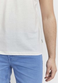 Bijela pamučna majica s okruglim izrezom, kratkim rukavima i šivenim rubom; uparena s svijetloplavim trapericama. Značajna oznaka s strane.