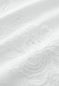 Witte geborduurde stof met intricat florale patronen. De textuur lijkt zacht met een lichte glans, waardoor het gedetailleerde ontwerp wordt versterkt.