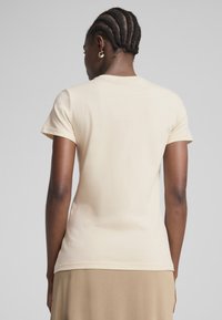 Cremefarvet kortærmet t-shirt lavet af bomuld, med et enkelt design og en tætsiddende silhuet. Synlige sømdetaljer langs kanterne.