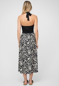 Haut dos nu noir avec un dos noué, associé à une longue jupe à motif zèbre noir et blanc ; tissu lisse et design fluide.