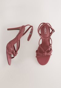 Sandales à talons hauts de couleur rose poudré avec des brides tressées et un détail de boucle. Texture lisse avec un design à bout ouvert et talon effilé.