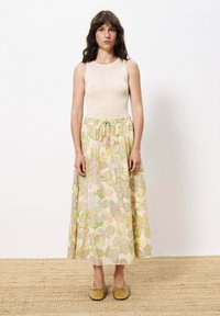 Beiger gerippter Tanktop, maxilanger Rock mit floralen Mustern in Gelb, Pink und Grün, verstellbarer Bund und braunen Slippern.