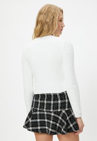 Biała swetrowa bluza o fakturze, z długimi rękawami, w połączeniu z czarno-białą spódnicą w kratę typu skater, z rozszerzanym dołem i usztywnioną talią.