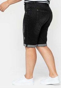 Black denim shorts with a rolled hem, featuring light distressing on the front. Paired with white sneakers, displayed from the side.