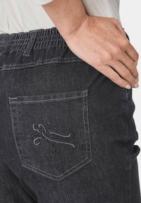 Donkerdenim broek met een elastische tailleband, voorzien van een achterzak geborduurd met een decoratief design. Getextureerde stof met een lichte glans.