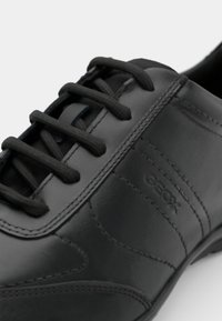 Pantof de piele neagră cu șireturi, având o textură netedă, cu cusături în contrast și un mic logo pe lateral.
