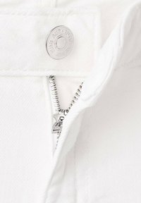 Un tissu en denim blanc présentant un bouton argenté avec "AUTHENTIC" gravé, ainsi qu'une fermeture éclair métallique avec des dents visibles.