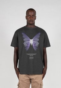 Mørkegrå bomulds t-shirt med et stort lilla sommerfugl grafik og tekst nedenfor. Korte ærmer og en afslappet pasform.