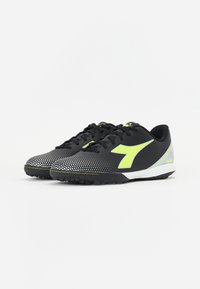Zapatillas deportivas negras con acentos en amarillo neón, parte superior de malla texturizada, patrón de puntos en la parte delantera y suela de goma diseñada para el agarre.