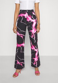 Calças de ganga com boca de sino, apresentando uma base negra com um padrão de relâmpago em rosa e branco, de cintura alta com fecho de botão, combinadas com saltos cor-de-rosa.