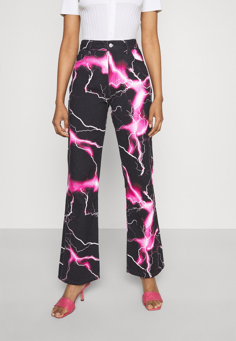 Calças de ganga com boca de sino, apresentando uma base negra com um padrão de relâmpago em rosa e branco, de cintura alta com fecho de botão, combinadas com saltos cor-de-rosa.