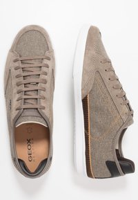 Sneaker in suede e tessuto marrone con suola in gomma bianca, caratterizzate da cuciture arancioni e un contrastante accento marrone scuro sul tallone.