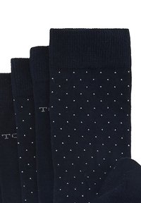 Marinblå strumpor med små vita prickar, ribbade muddar och en slät textur. Fyra par visade, vikta med logotyper nära toppen.