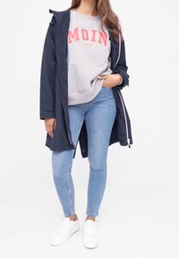 Marinparkas med huva, grå sweatshirt med "MOIN"-tryck, ljusblå slim-fit jeans och vita sneakers. Synlig ljusrosa dragkedjedetalj.