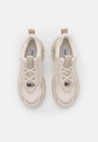 Béžové tenisky s síťovaným svrškem, texturovanými akcenty a robustní gumovou podrážkou. Mají logo na jazyku a detaily šněrování.