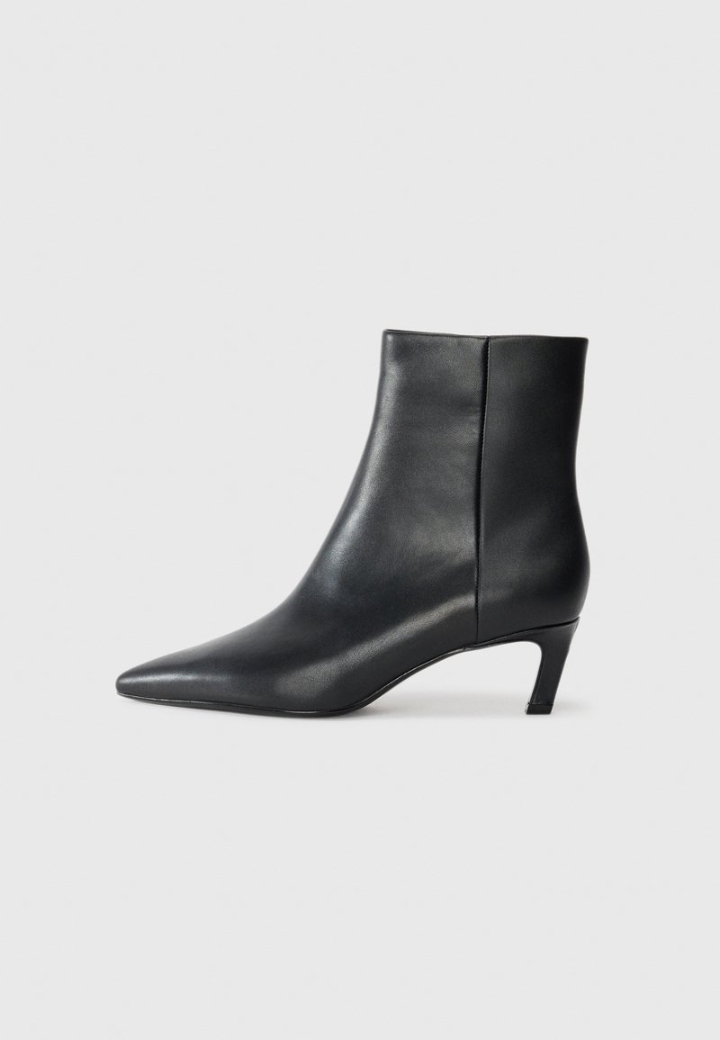 Black leather ankle boot with pointed toe and low kitten heel on a plain light background.