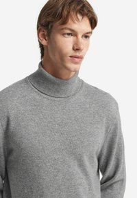 Grauer Rollkragenpullover aus weichem Strickstoff. Mit engem Kragen, langen Ärmeln und einem lässigen Schnitt, der eine dezente Struktur aufweist.