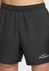 Schwarze Sportshorts mit einem elastischen Bund, glatter Textur und silbernem Nike-Logo auf der unteren rechten Seite. Kurz geschnittenes Design.