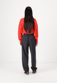 Red cropped sweatshirt with long sleeves, paired with dark gray high-waisted trousers featuring back pockets and elastic cuffs.