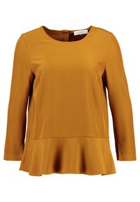 Top giallo senape a maniche lunghe con scollatura rotonda e orlo peplum svasato. Realizzato in tessuto morbido con fessure laterali per facilitare i movimenti.
