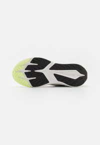 A Nike cipőtalpa textúrás fekete gumiból készült, élénk sárga-zöld kiemeléssel rendelkezik, amely a tapadás mintáit és a légies formatervezést emeli ki.