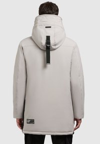 Cămașă izolată de culoare gri deschis, cu guler înalt, glugă captusită și detalii cu curea neagră. Prezintă o etichetă pe partea stângă jos.