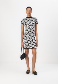 Svart-hvitt kortermet kjole med blomstermønster. Modellen holder en liten svart veske og har på seg svarte spisse ballerinas. Enkelt design.