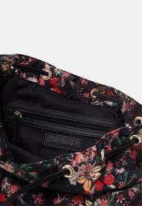 Blomstermönstrad tygkasse med svart inredning, som har en dragkedjeficka och guldiga metalldetaljer för stängning.