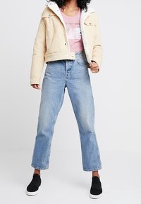 Beige kordurojová bunda s bílou fleecovou podšívkou, růžové tričko s potiskem, modré rovné džíny a černé slip-on boty.